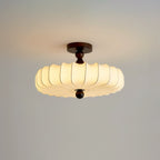 On a soft grey backdrop, a lit Clérachic ceiling light glows warm, its fabric ribs layered at the scalloped edge.