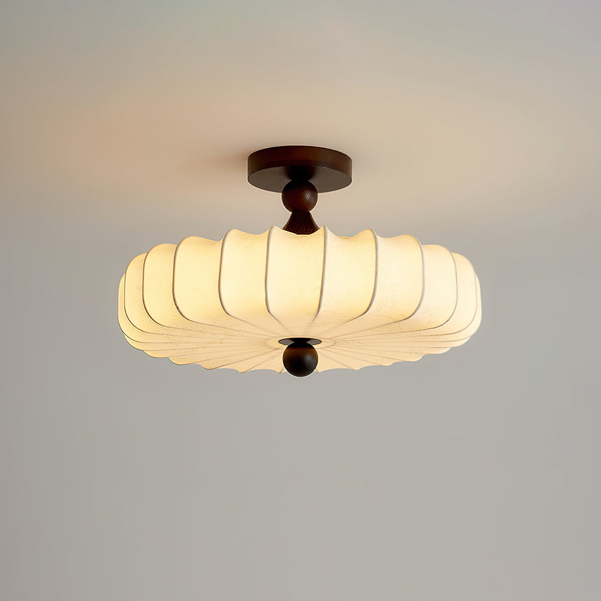 A lit Clérachic ceiling light with a wide pleated shade hangs on a pale grey backdrop, a small round finial below.