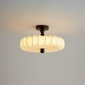 A glowing Clérachic ceiling light with a pleated shade and dark canopy, set against a pale grey-blue backdrop.
