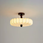 A glowing Clérachic ceiling light with a pleated shade and dark canopy, set against a pale grey-blue backdrop.