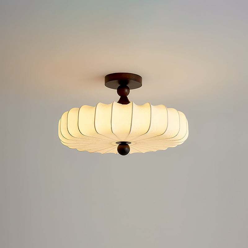 A glowing Clérachic ceiling light with a pleated shade and dark canopy, set against a pale grey-blue backdrop.