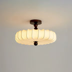 A Clérachic ceiling light with a wide, lit pleated shade and a dark walnut-colour stem hangs against a grey backdrop.