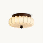 A pleated fabric Clérachic ceiling light, with a dark walnut-coloured frame and a wooden ball at the centre, on white.
