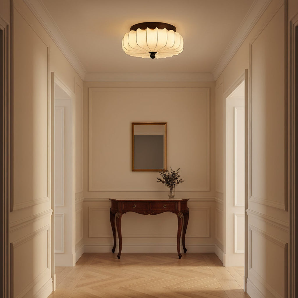 A pleated fabric Clérachic ceiling light lit above a panelled hallway, with a carved wooden console and a small mirror.
