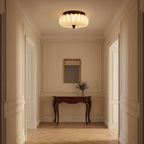 A pleated fabric Clérachic ceiling light lit above a panelled hallway, with a carved wooden console and a small mirror.