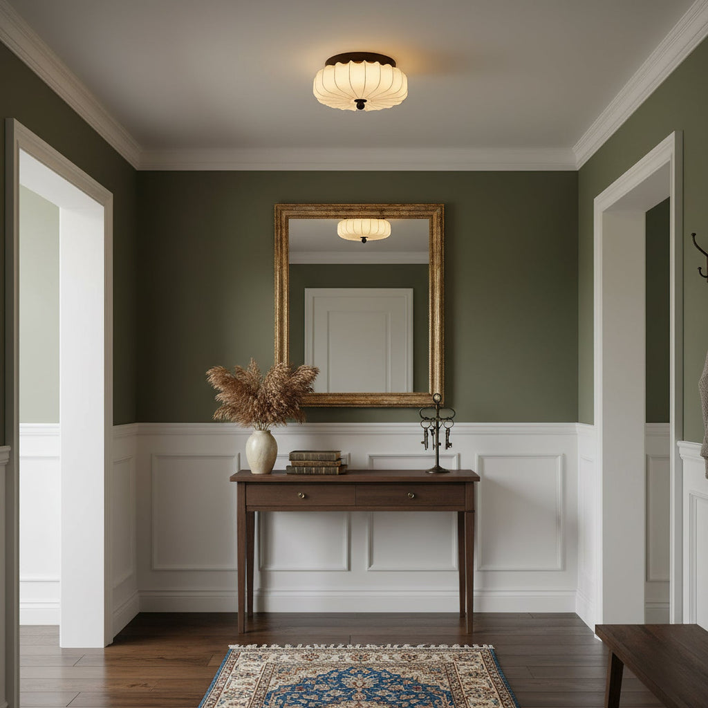 Over a hallway with olive walls, a gilt mirror and a wooden console, this pleated Clérachic ceiling light gives a warm glow.