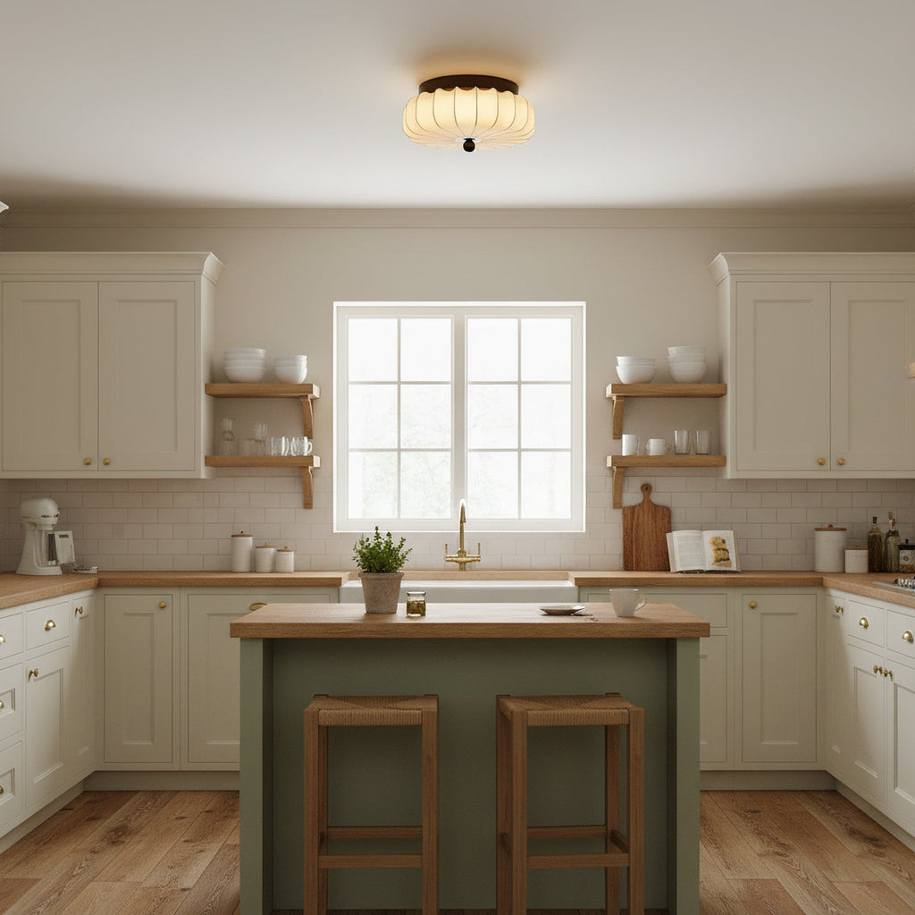 Over a cream kitchen with a green island and two wooden stools, this pleated fabric Clérachic ceiling light is lit.