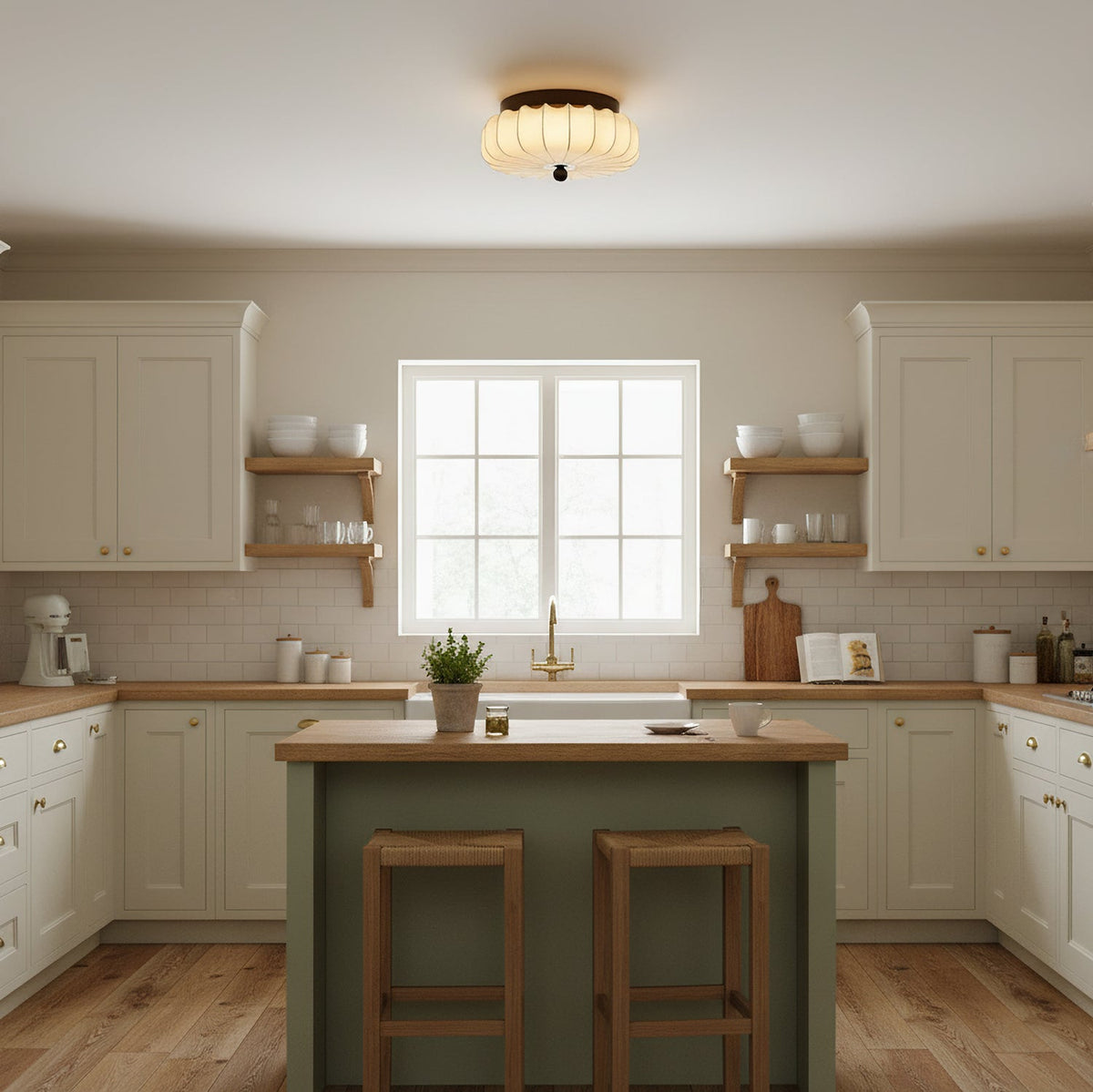 Over a cream kitchen with a green island and two wooden stools, this pleated fabric Clérachic ceiling light is lit.