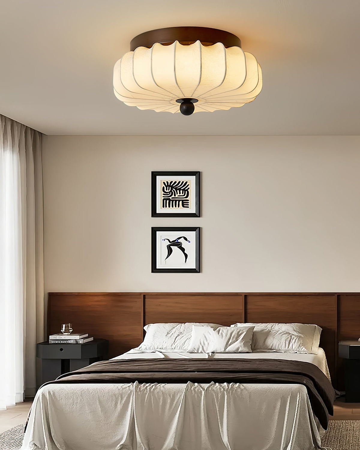 Above a made bed with a walnut headboard and two small framed prints hangs this pleated fabric Clérachic ceiling light.