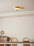 A small Clérachic ceiling light lit warm above a dining room with a long table, carved-back chairs and a cornice.