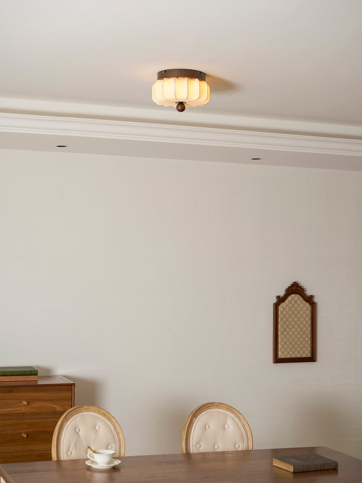 A small pleated Clérachic ceiling light lit in a dining room, above a table with cups and a walnut sideboard.