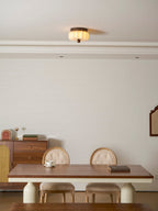 A pleated Clérachic ceiling light lit above a dining table with cream pedestals, chairs and a walnut sideboard.