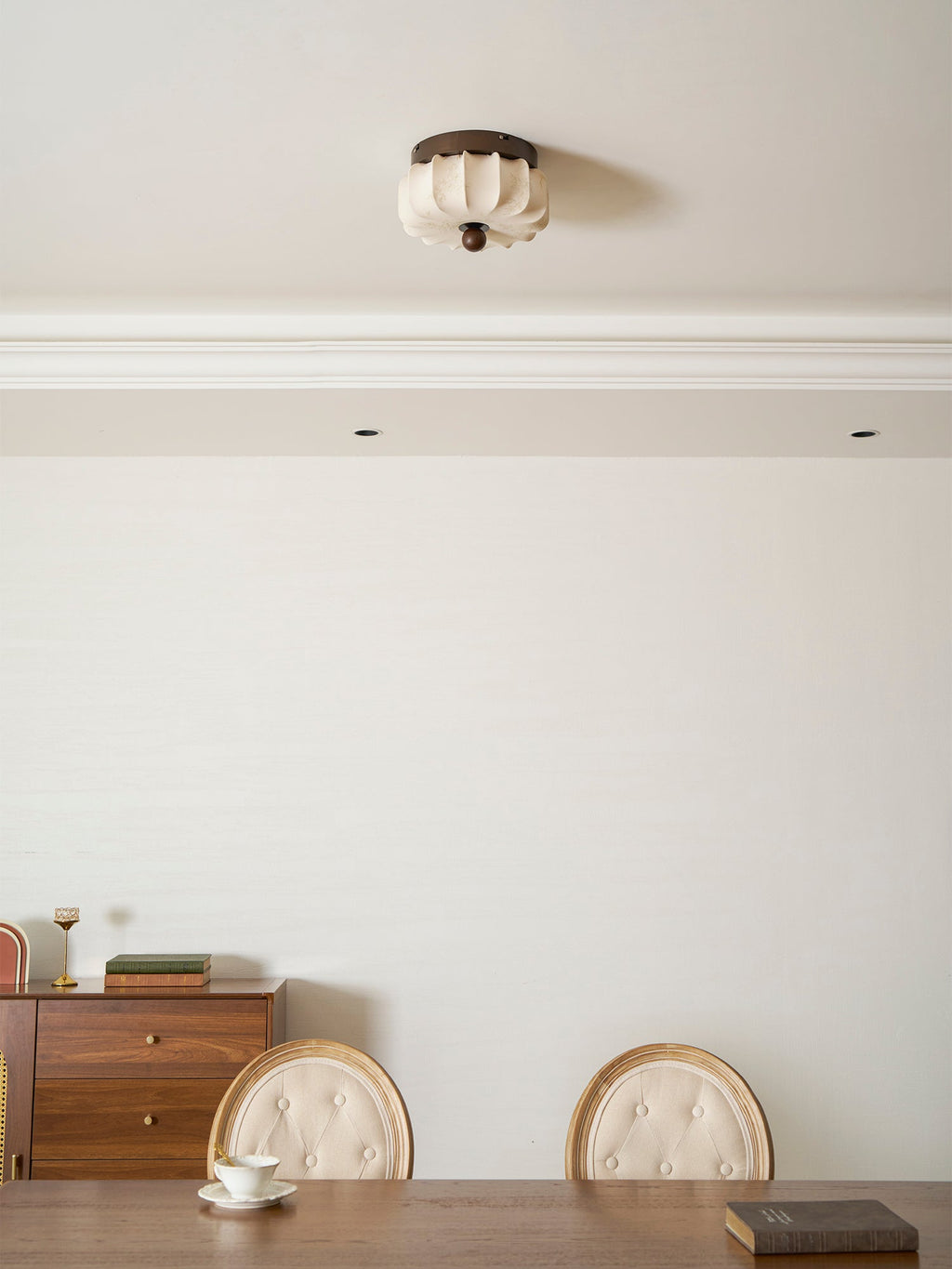 A pleated Clérachic ceiling light, unlit, above a dining room with a sideboard, a table and button-backed chairs.