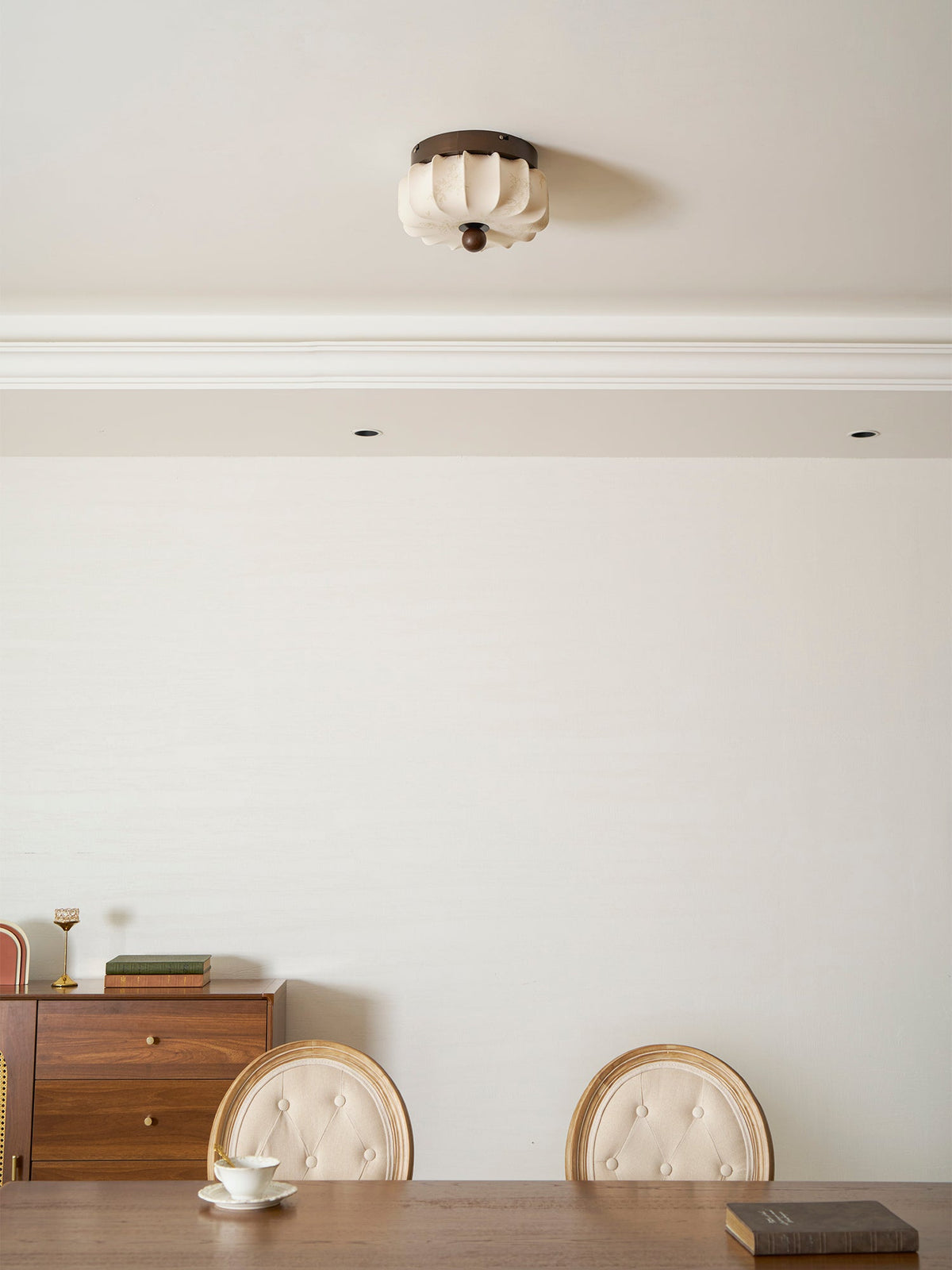 A pleated Clérachic ceiling light, unlit, above a dining room with a sideboard, a table and button-backed chairs.