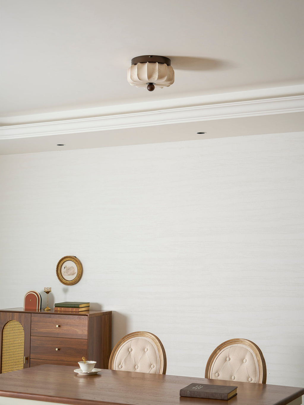 A pleated Clérachic ceiling light, unlit, in a dining room with a cornice, a sideboard and a small round mirror.