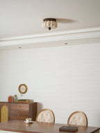 A pleated Clérachic ceiling light, unlit, in a dining room with a cornice, a sideboard and a small round mirror.