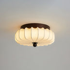 A wider pleated fabric Clérachic ceiling light lit, with a dark walnut frame and a wooden ball, against a grey ceiling.