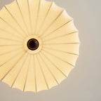 View from below of the ribbed fabric shade on this Clérachic ceiling light, lit, with a wooden ball at the centre.