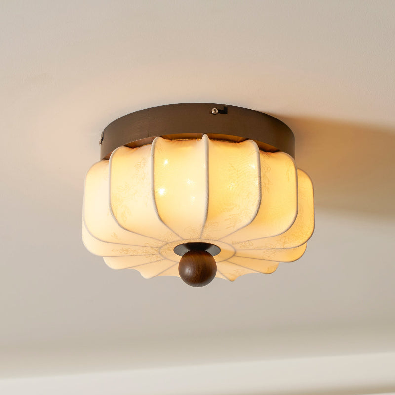 A pleated fabric Clérachic ceiling light lit warm, with a dark walnut frame and a round wooden ball below.