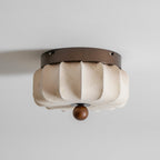 A pleated fabric Clérachic ceiling light, unlit, with a faint floral print on the fabric and a walnut ball below.