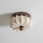 A pleated fabric Clérachic ceiling light, unlit, with a folded shade and a faint floral print, on a grey ceiling.