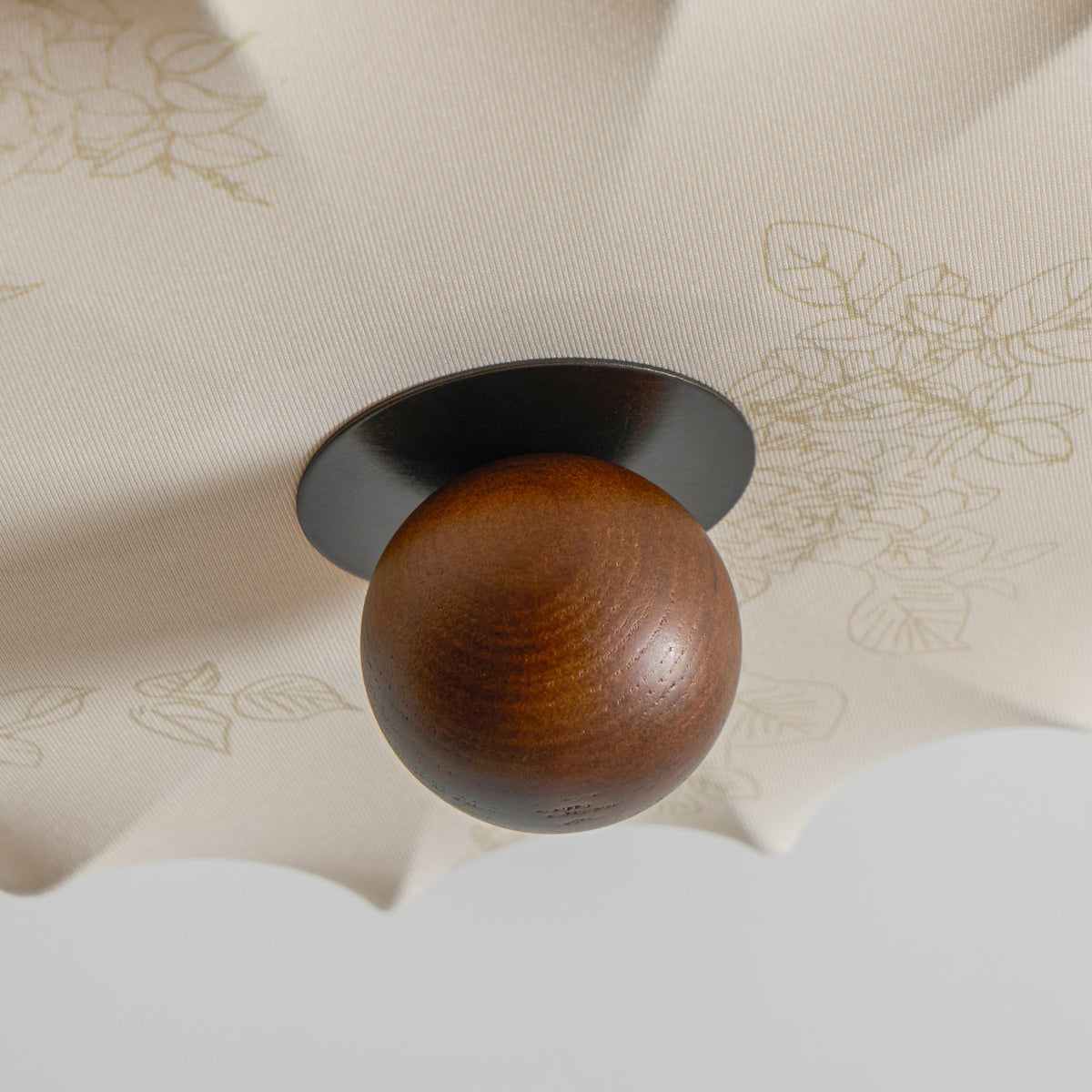 Close view of the walnut ball and a faint floral print on the fabric of this Clérachic ceiling light.