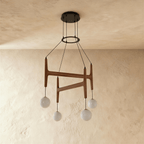 A side view of the Clérachic chandelier in mahogany wood, its four frosted globes glowing on black cords.