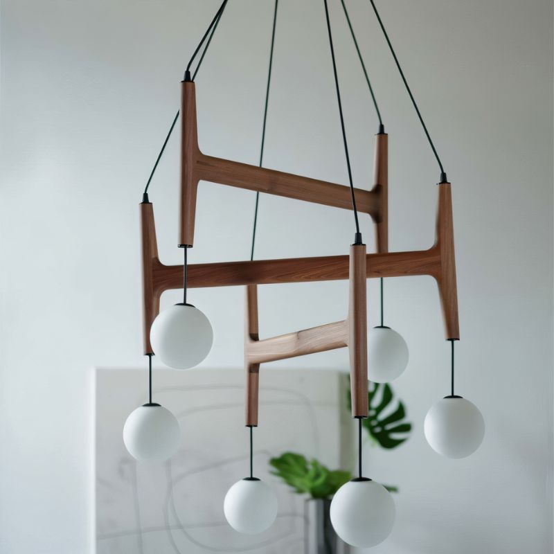 Clérachic's chandelier in mahogany wood, its six frosted globes glowing above a sideboard with a plant.