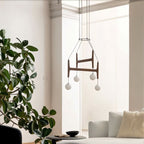 Clérachic's chandelier in black walnut wood, its four frosted globes glowing in a bright room with plants.