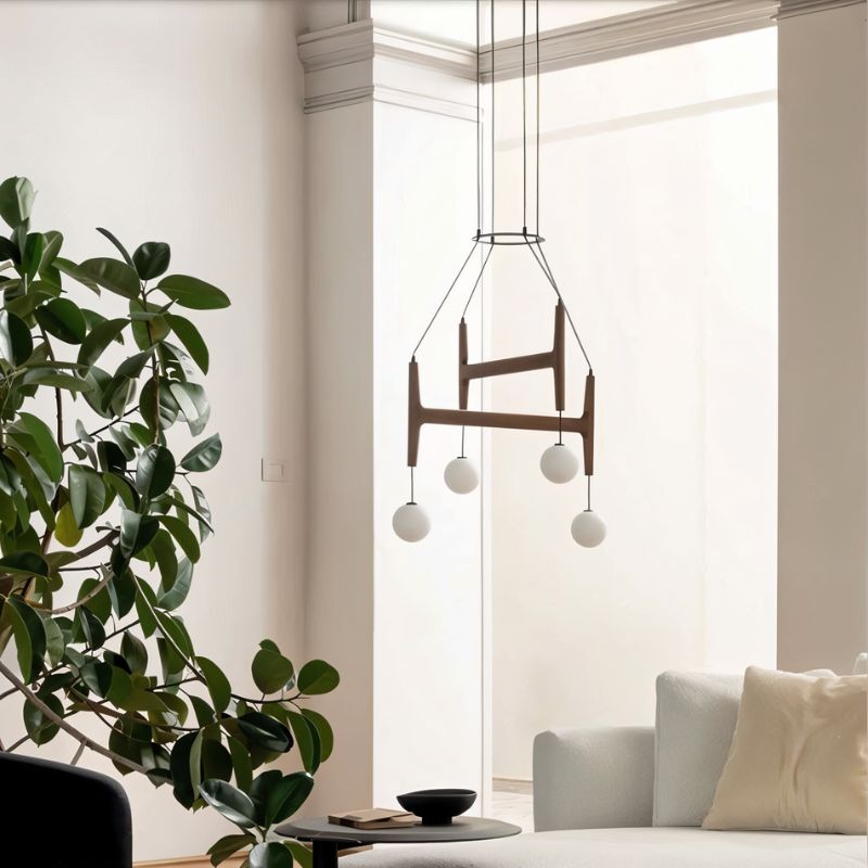 Clérachic's chandelier in black walnut wood, its four frosted globes glowing in a bright room with plants.