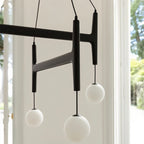 A close detail of the Clérachic chandelier's black walnut frame and frosted globes beside a garden window.