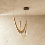 Clérachic chandelier of three boomerang-shaped oak loops in light wood, each lit along its edge, hung from a black canopy.