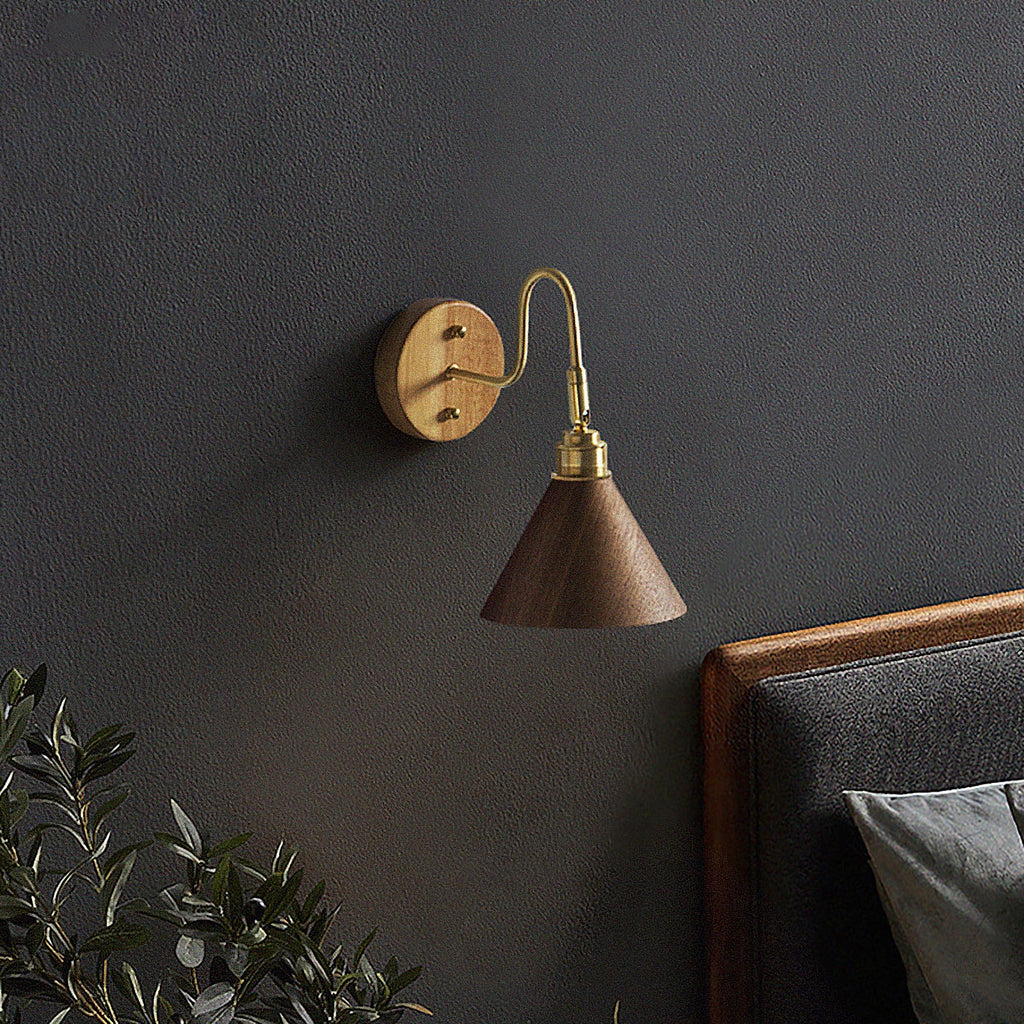 Small Clérachic wall light with a walnut-colour cone shade and brass arm on a dark charcoal wall above a leather headboard.