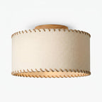 Angled view from below of a Clérachic linen drum ceiling light, its rope-trimmed rim and wood canopy against a pale backdrop.