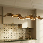 Clérachic wavy wood-finish chandelier in close-up, its warm LED line tracing the curves above a patterned tile kitchen splashback.