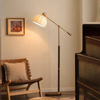 Lit Clérachic floor lamp in a warm beige corner, its pleated shade glowing beside a woven wooden chair and a framed print.