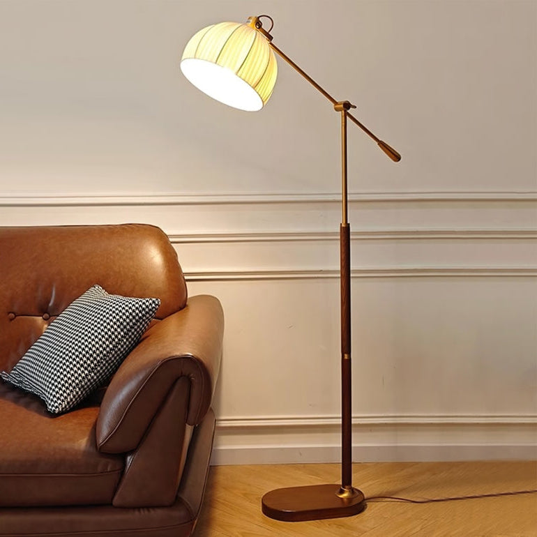 Pleated beige shade of this Clérachic floor lamp glowing above a tan leather sofa with a checked cushion, on a pale wood floor.