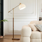 Clérachic arc floor lamp in a white panelled room, the beige shade lit above a curved boucle armchair and a leafy plant.