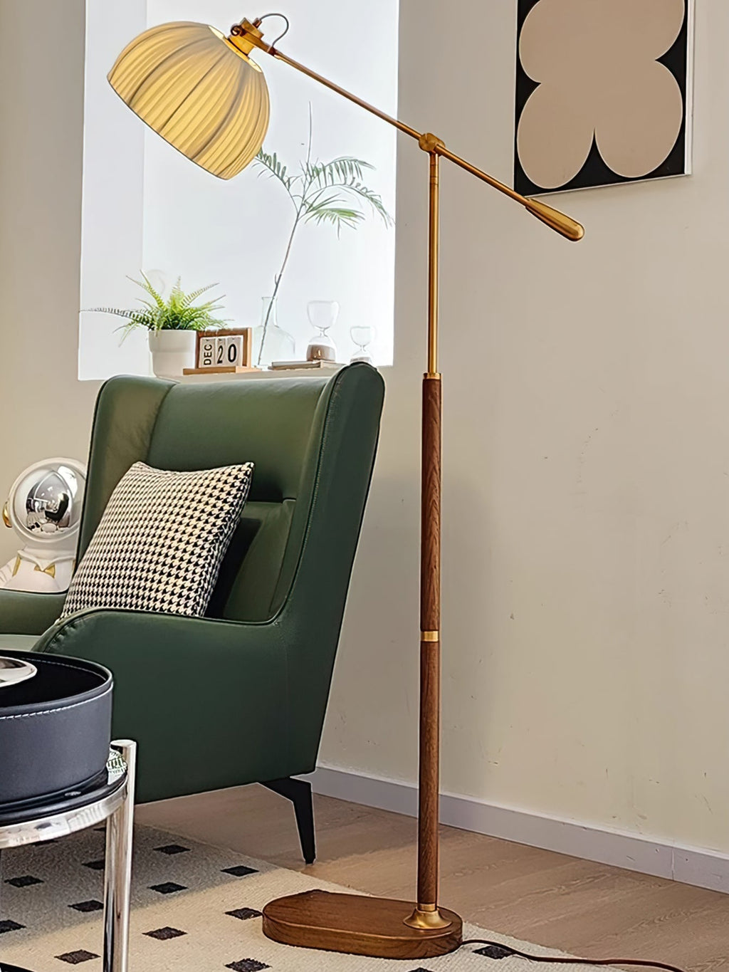 A Clérachic floor lamp beside a green wingback armchair with a houndstooth cushion, with a leafy plant on the sill behind.