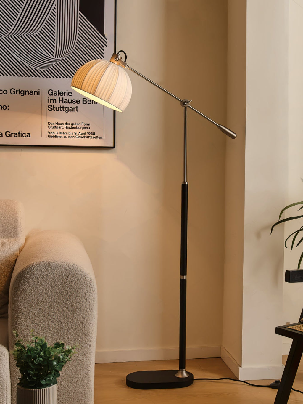 Black-stemmed Clérachic floor lamp with a pleated beige shade, standing beside a cream armchair under a framed poster.