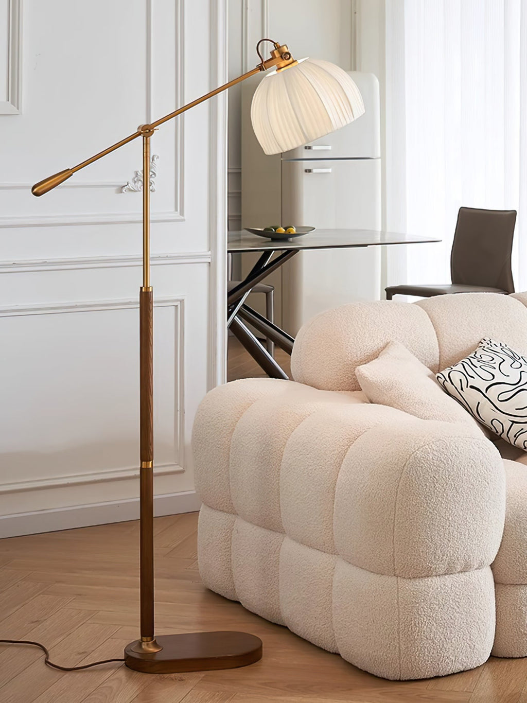 Clérachic floor lamp rising behind a quilted cream sofa in a bright room, with a glass table and dark chair in the background.