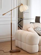 Clérachic floor lamp rising behind a quilted cream sofa in a bright room, with a glass table and dark chair in the background.