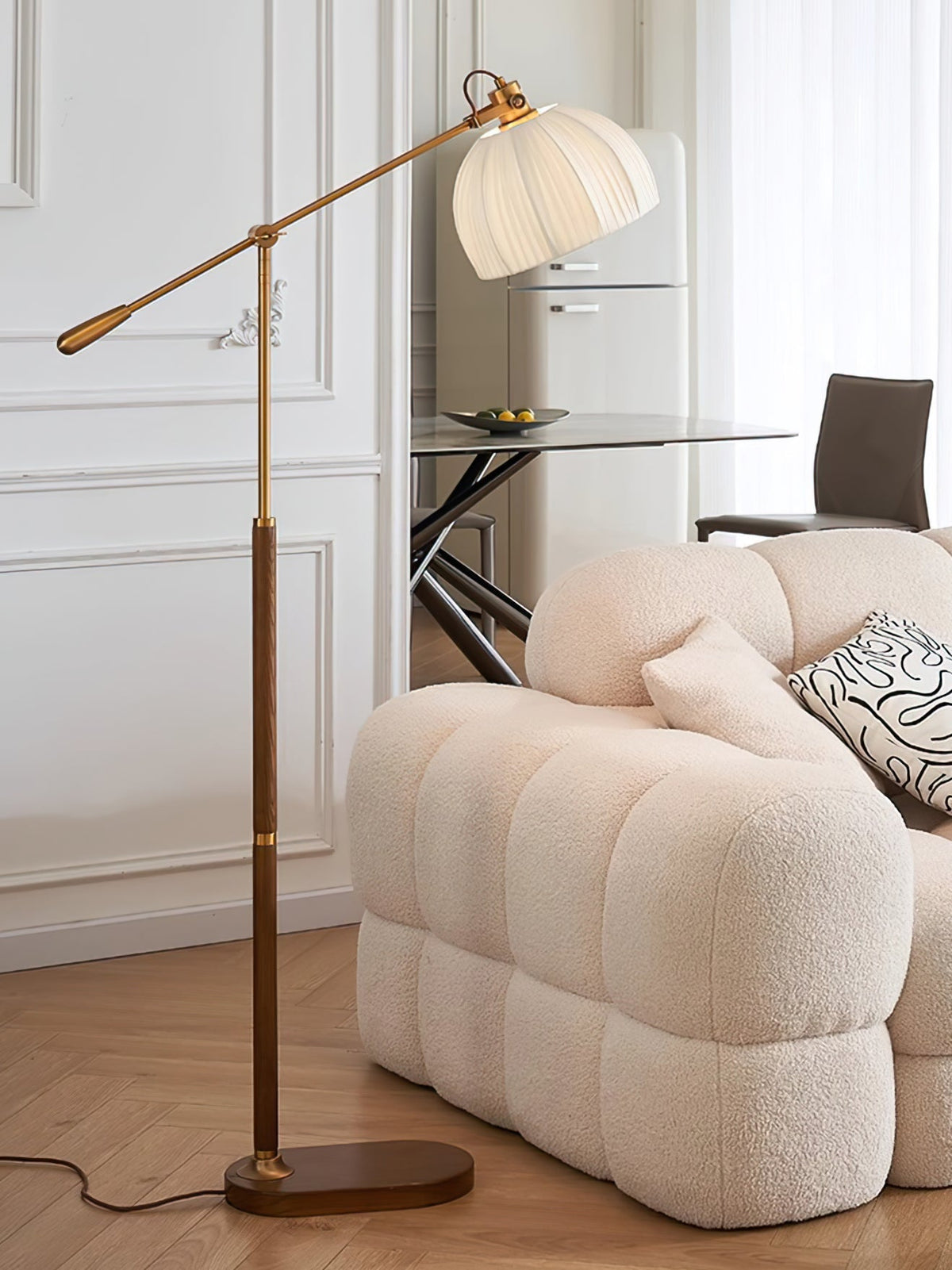 Clérachic floor lamp rising behind a quilted cream sofa in a bright room, with a glass table and dark chair in the background.