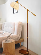 Clérachic floor lamp in a corner with a pale sofa and a rounded wooden stool holding a tablet, the arm stretched over the room.