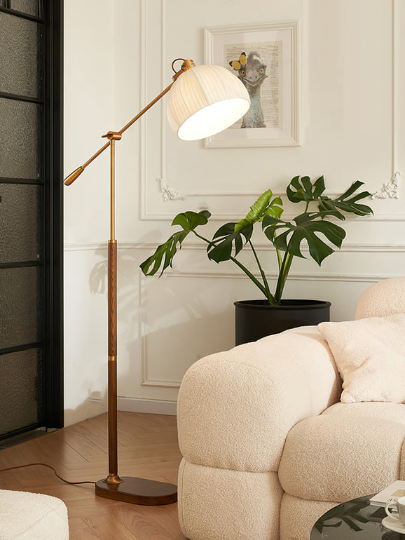 This Clérachic floor lamp has its shade angled down beside a monstera plant and a cream boucle sofa, with a framed print behind.