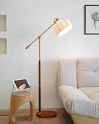 Clérachic floor lamp next to a sculptural wooden stool with a tablet on it, with a pale textured sofa and a framed leaf print.