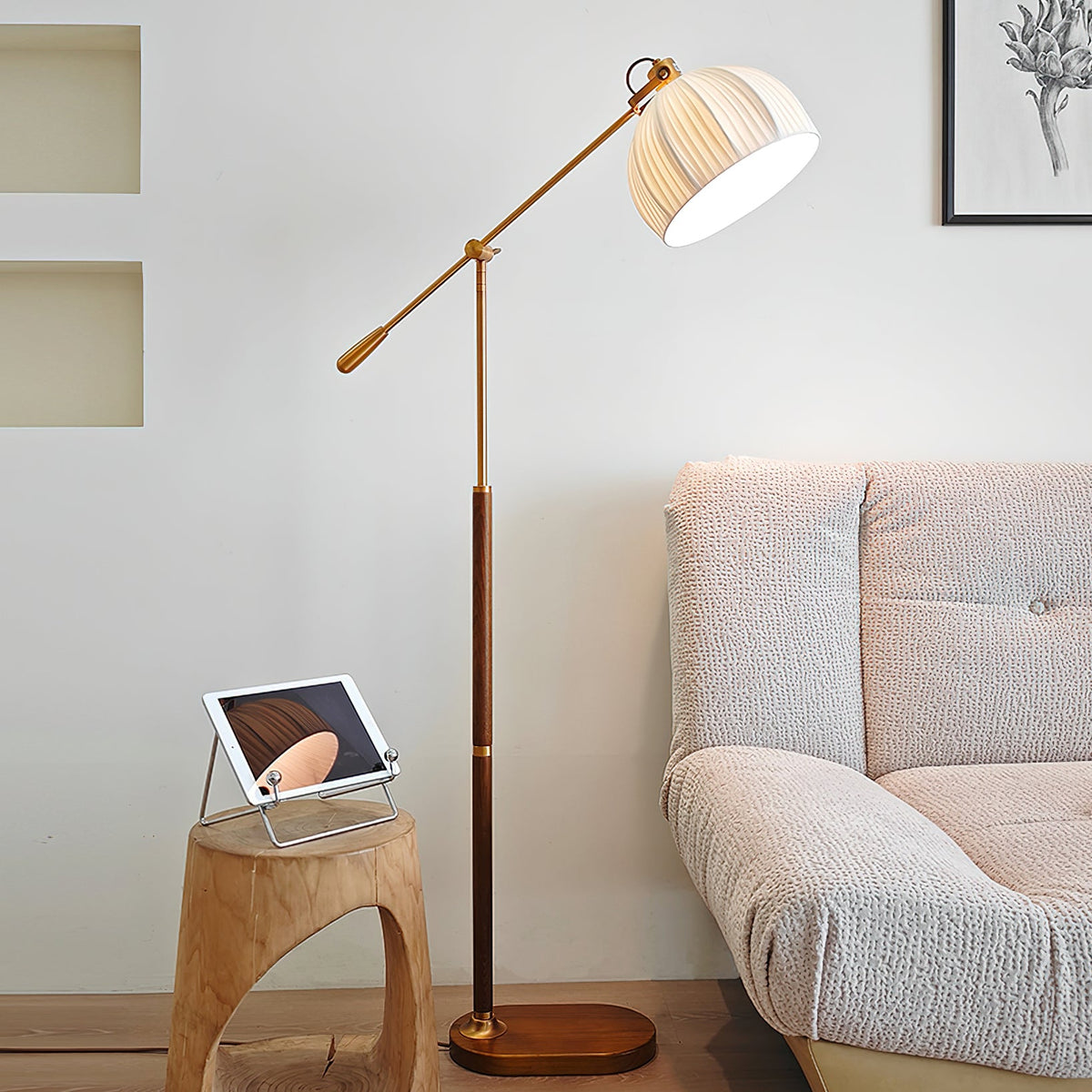Clérachic floor lamp beside a textured grey sofa and a hollow wooden stool with a tablet, the arm angled back from the wall.