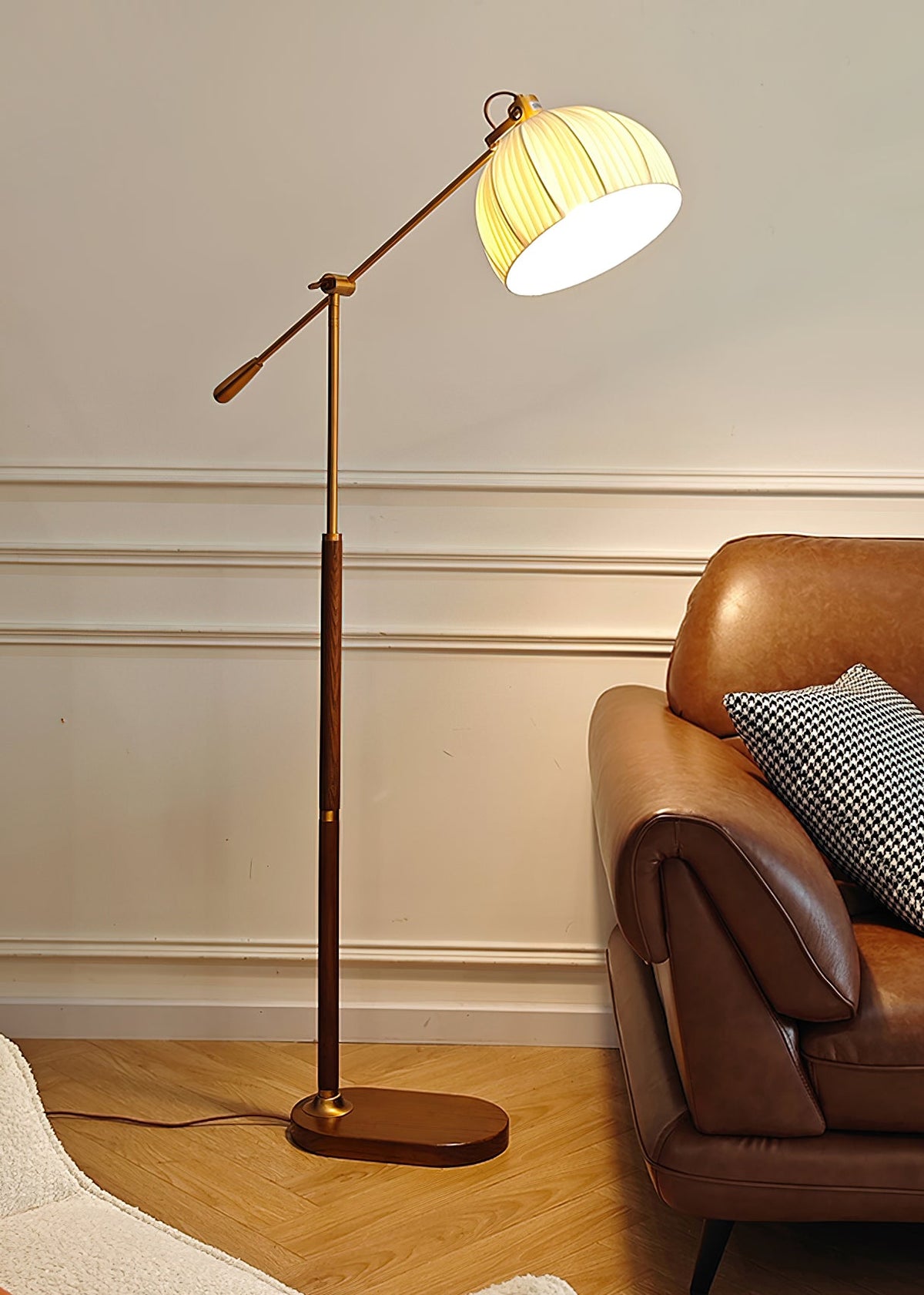 Clérachic floor lamp against a white wall with panel moulding, its shade glowing beside a tan leather armchair on herringbone flooring.