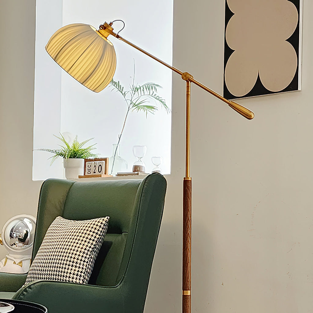 Close angle on the pleated shade and brass counterweight of this Clérachic floor lamp, above a green armchair and a small plant.