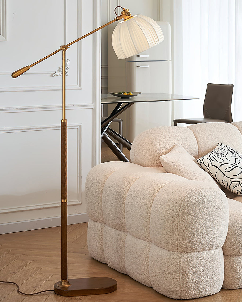 Clérachic floor lamp arching over a scalloped cream sofa on a herringbone floor, with a glass table and fridge in the background.